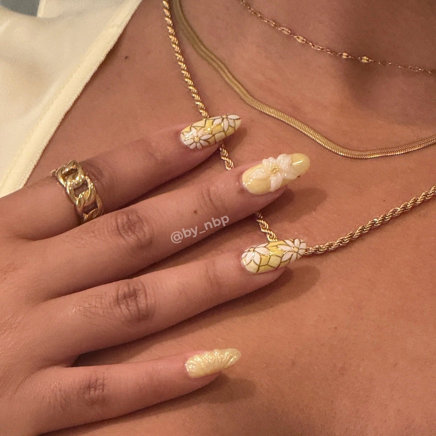 Client hand with almond shaped builder gel nails with glossy yellow & gold freestyle nail art to match a yellow outfit.