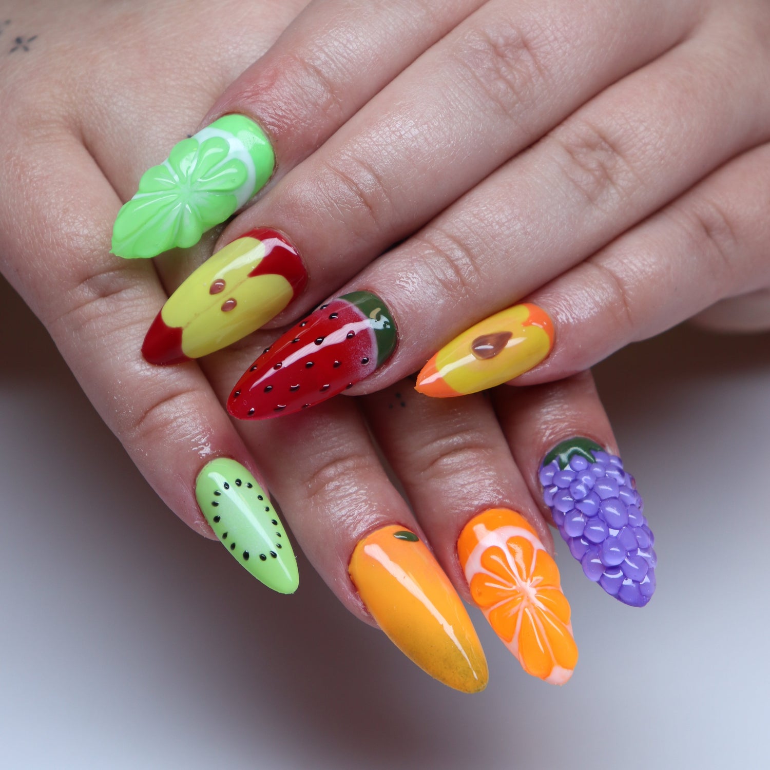 Client hands with medium almond gel-x extensions with 3D fruit inspired hand painted nail art.