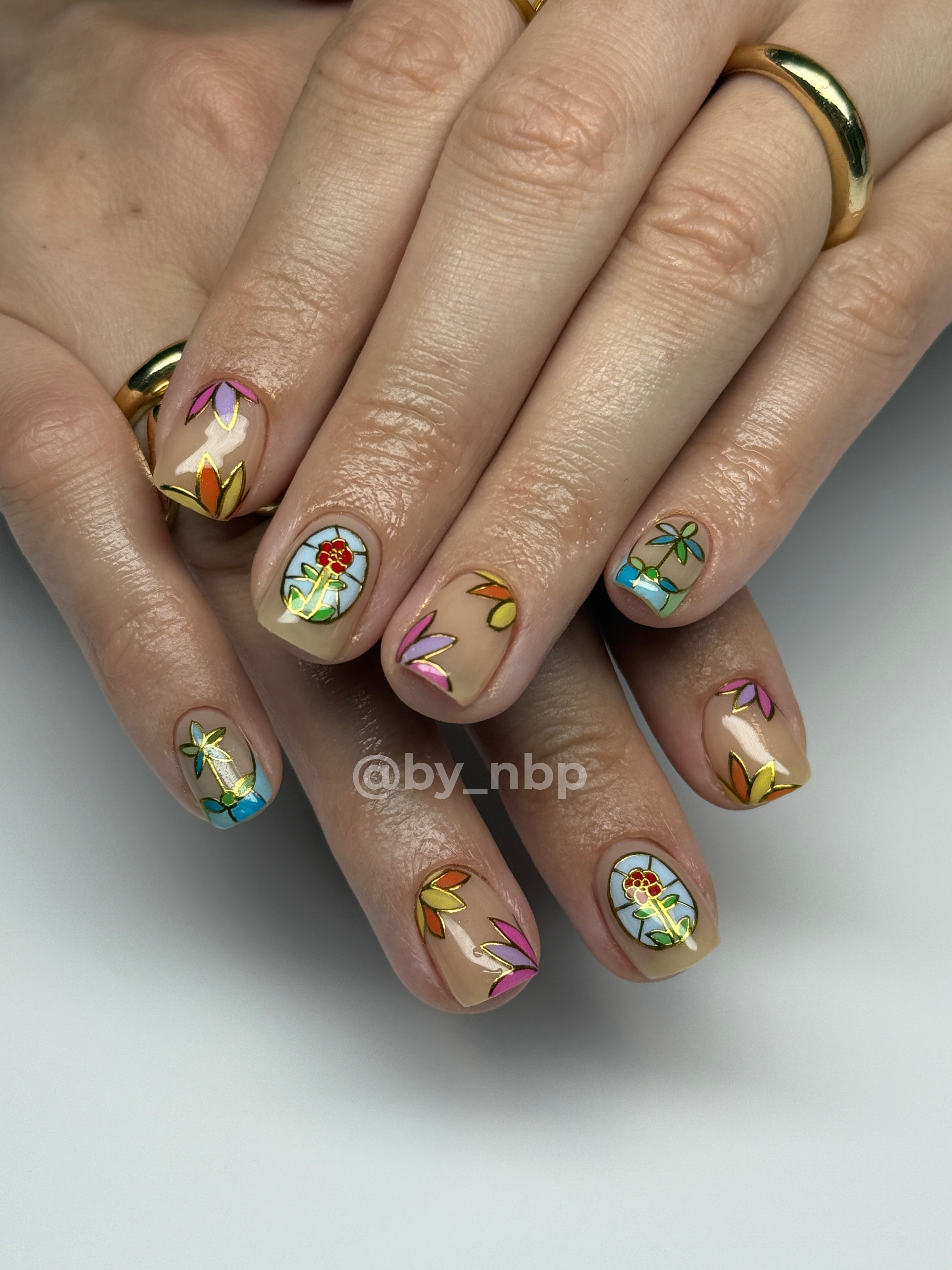 Client hands with short squoval shaped builder gel (BIAB) nails with stained glass nail art.