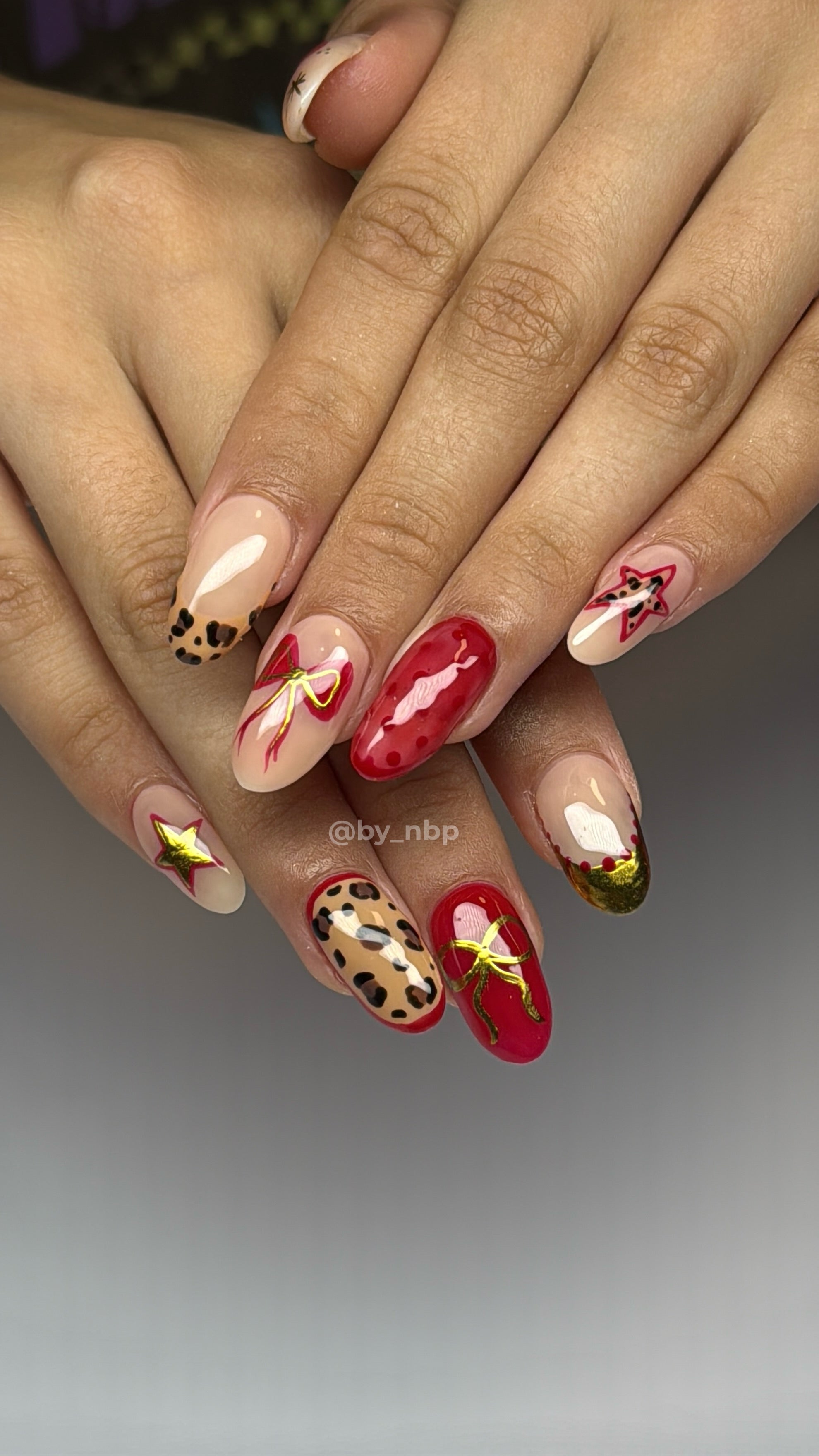 Client hand with almond shaped hard gel  nails with glossy red & gold freestyle nail art