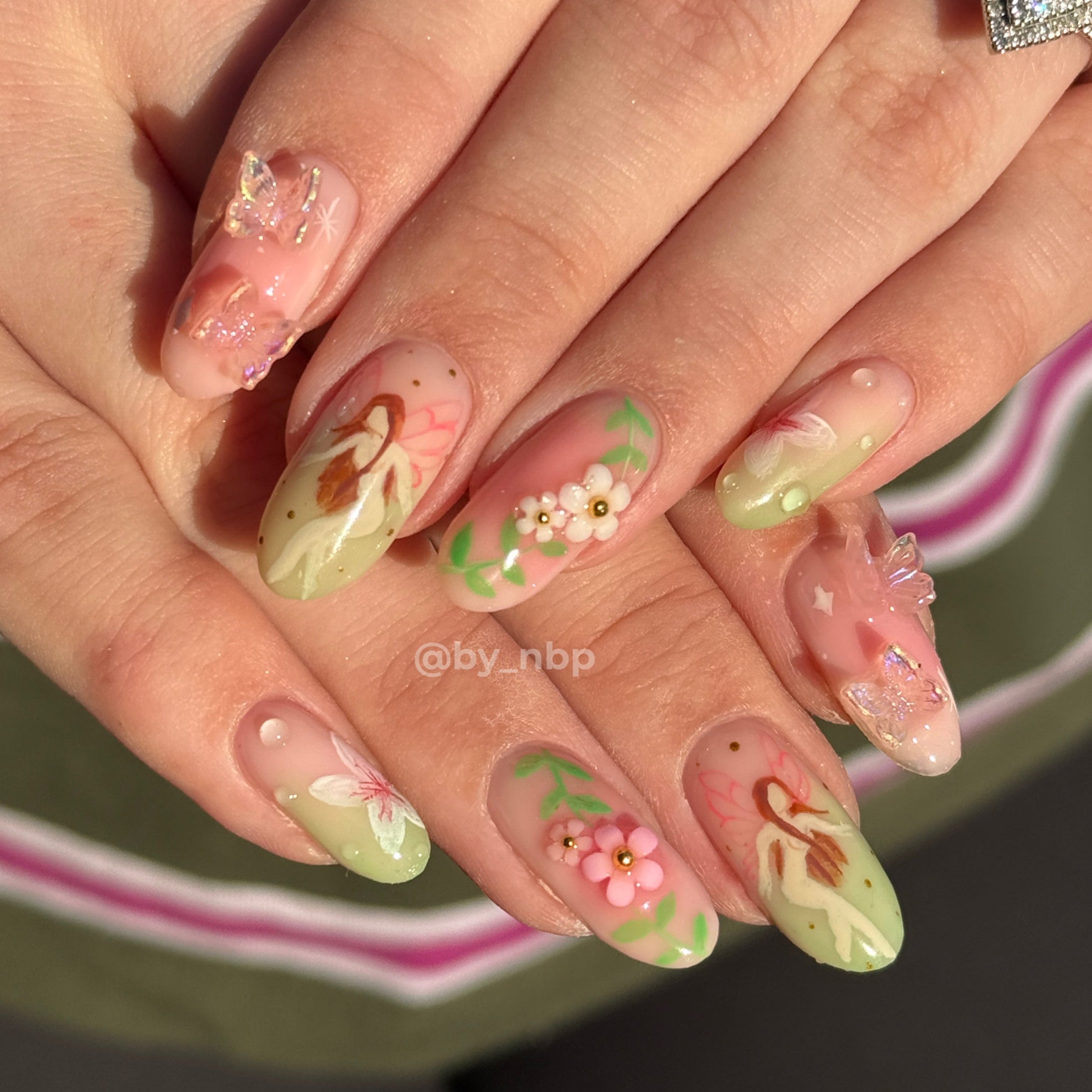 Client hands with long round shaped builder gel (BIAB) nails with freestyle fairy garden nail art.