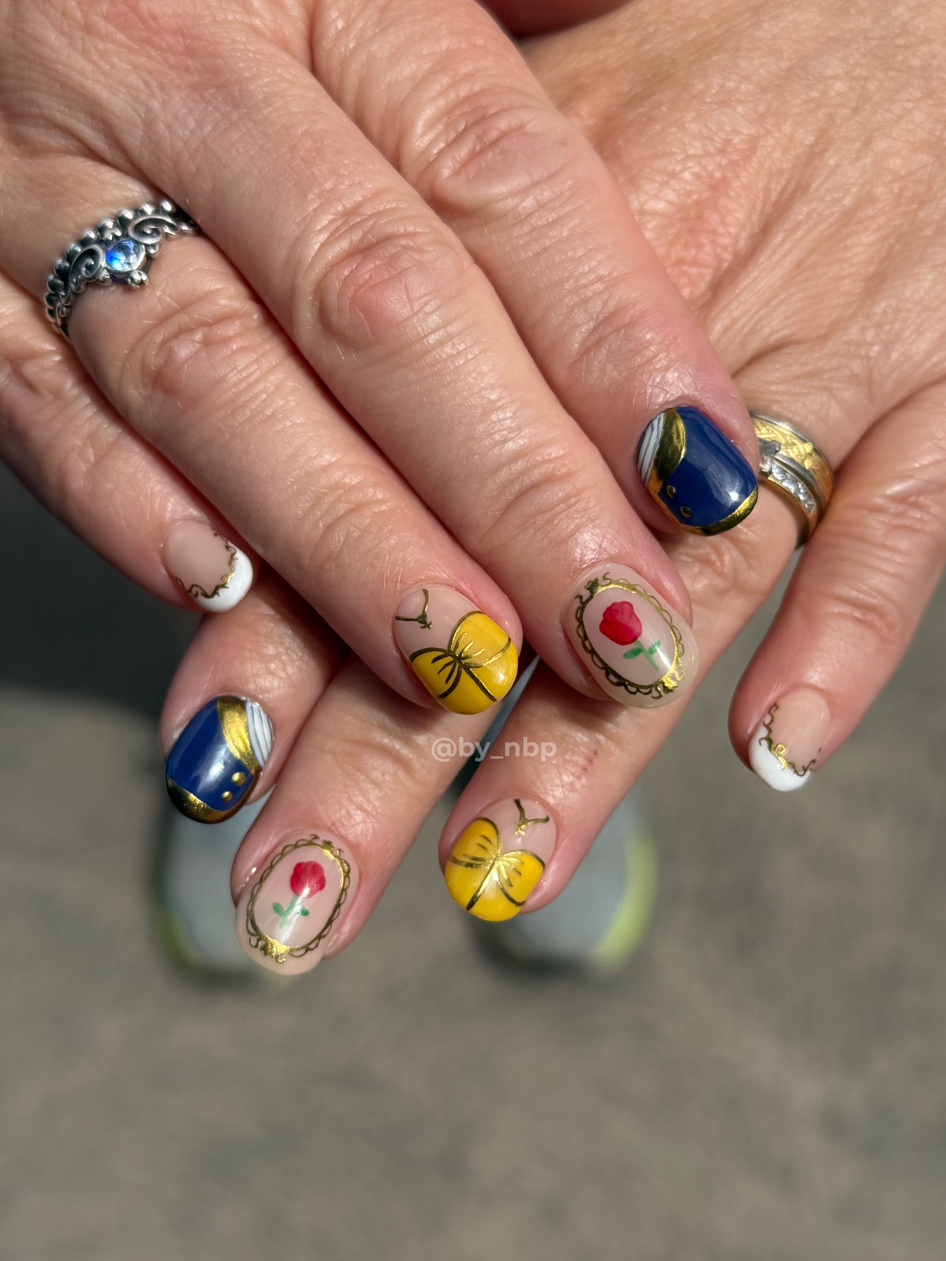 Client hand with round shaped builder gel (BIAB) nails with beauty & the beast inspired freestyle nail art.